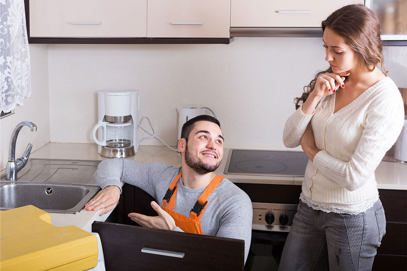 plumber working in kitchen with woman watching